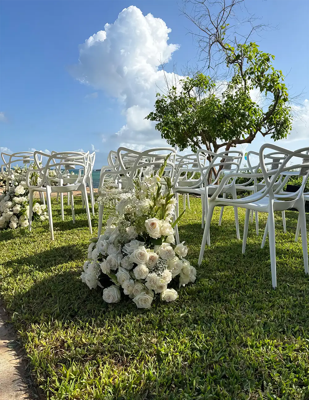Beach wedding ceremony setup with white chairs and floral arrangements overlooking the ocean