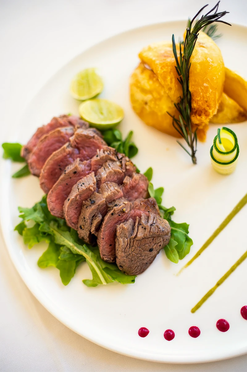 Gourmet dish of sliced grilled meat served with salad and roasted vegetables